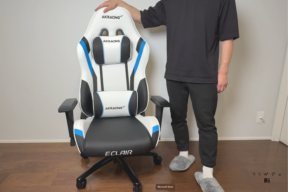 AKRacing Eclairゲーミングチェアにランバーサポートとヘッドレストを取り付けた状態。使用者が立った状態で全体サイズ感を確認している様子