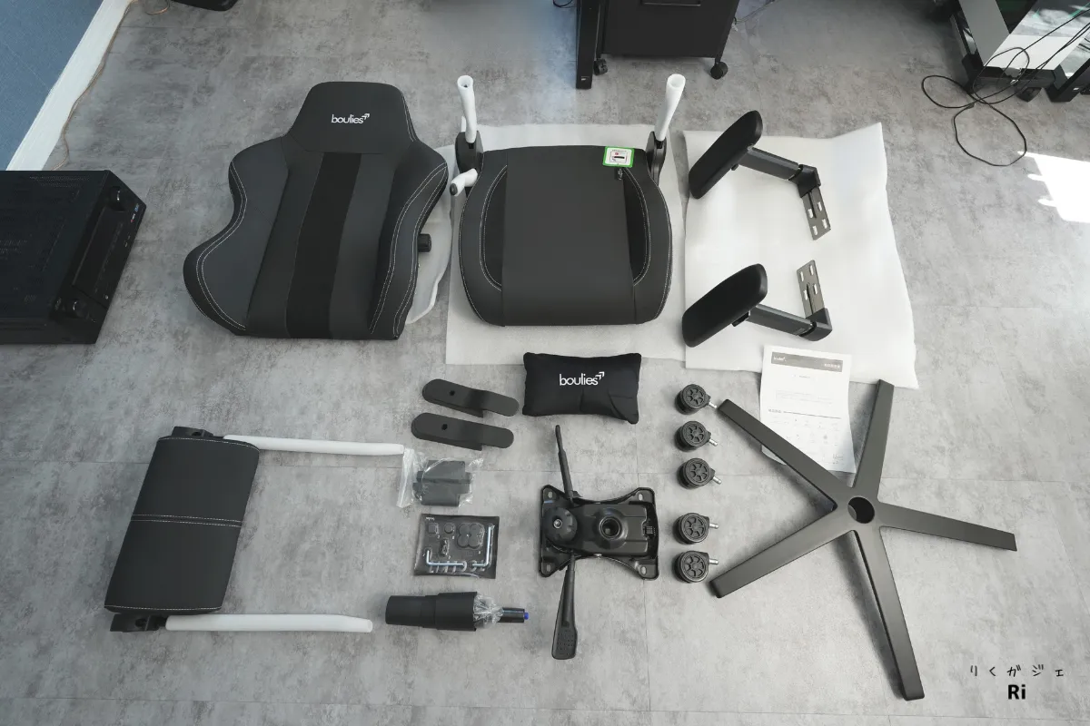 Boulies Master Rex の組み立て前パーツ一式が床に並べられている様子。背もたれ、座面、アームレスト、キャスター、ベースなどの構成部品が確認できる
