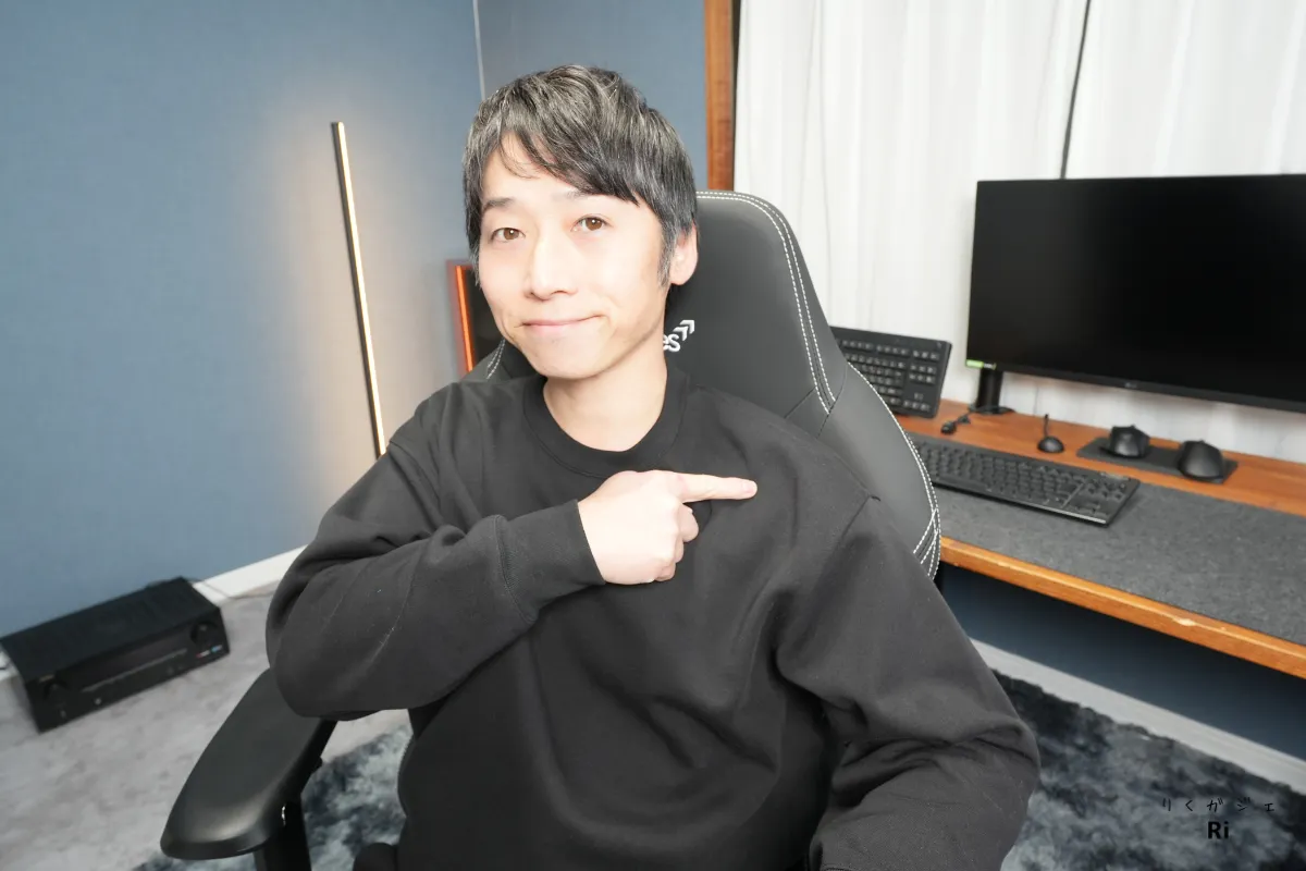 デスク前で椅子に座り、チェアの背もたれ部分を指さしている人物