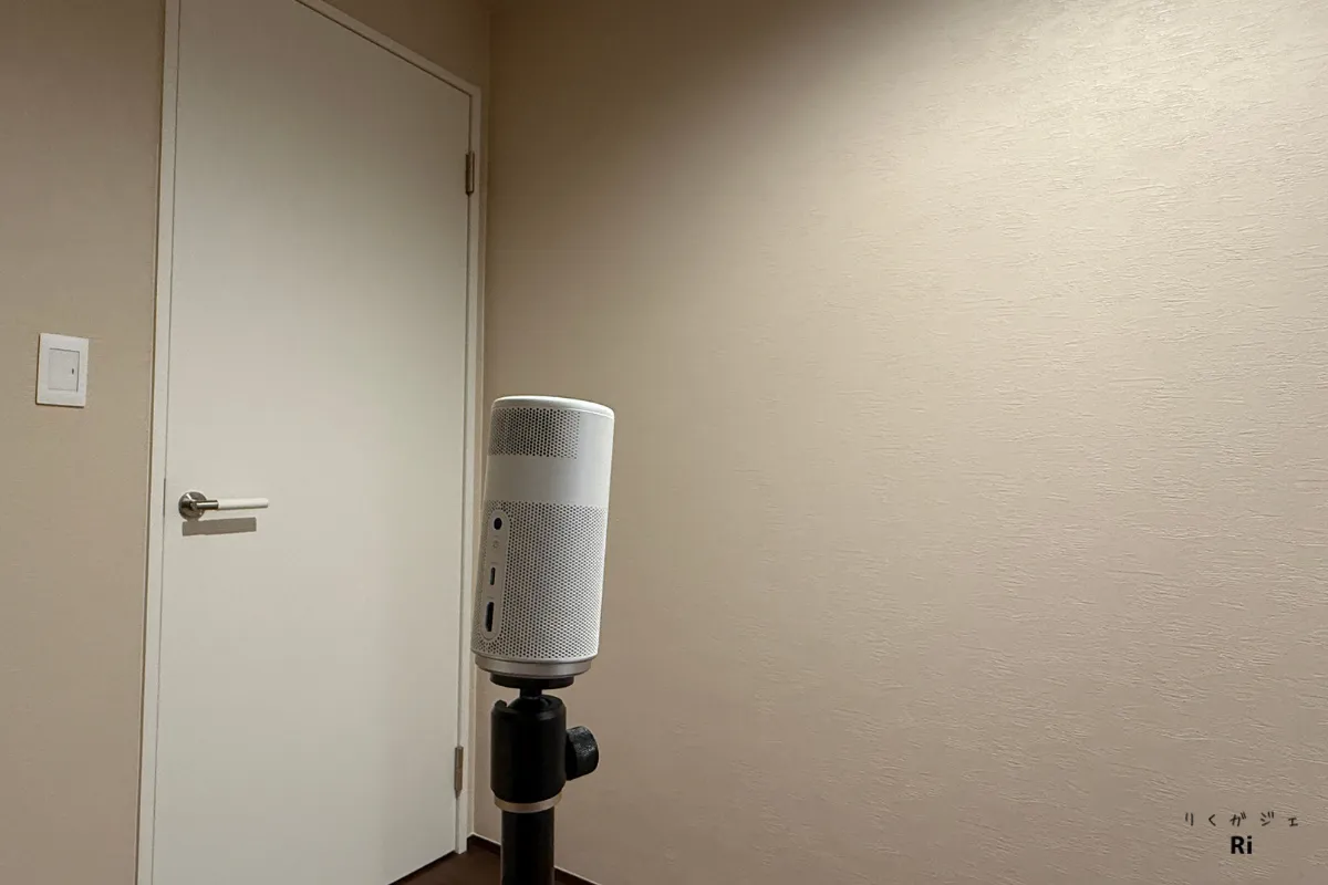 白い壁紙の部屋に設置されたNebula Capsule Air。ベージュ系の壁紙に対して、プロジェクター本体が三脚スタンドに取り付けられている。