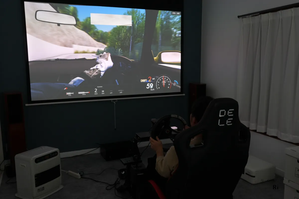 ハンコンとレーシングシートを使ってAssetto Corsaをプレイしている様子を投影映像とともに写した写真
