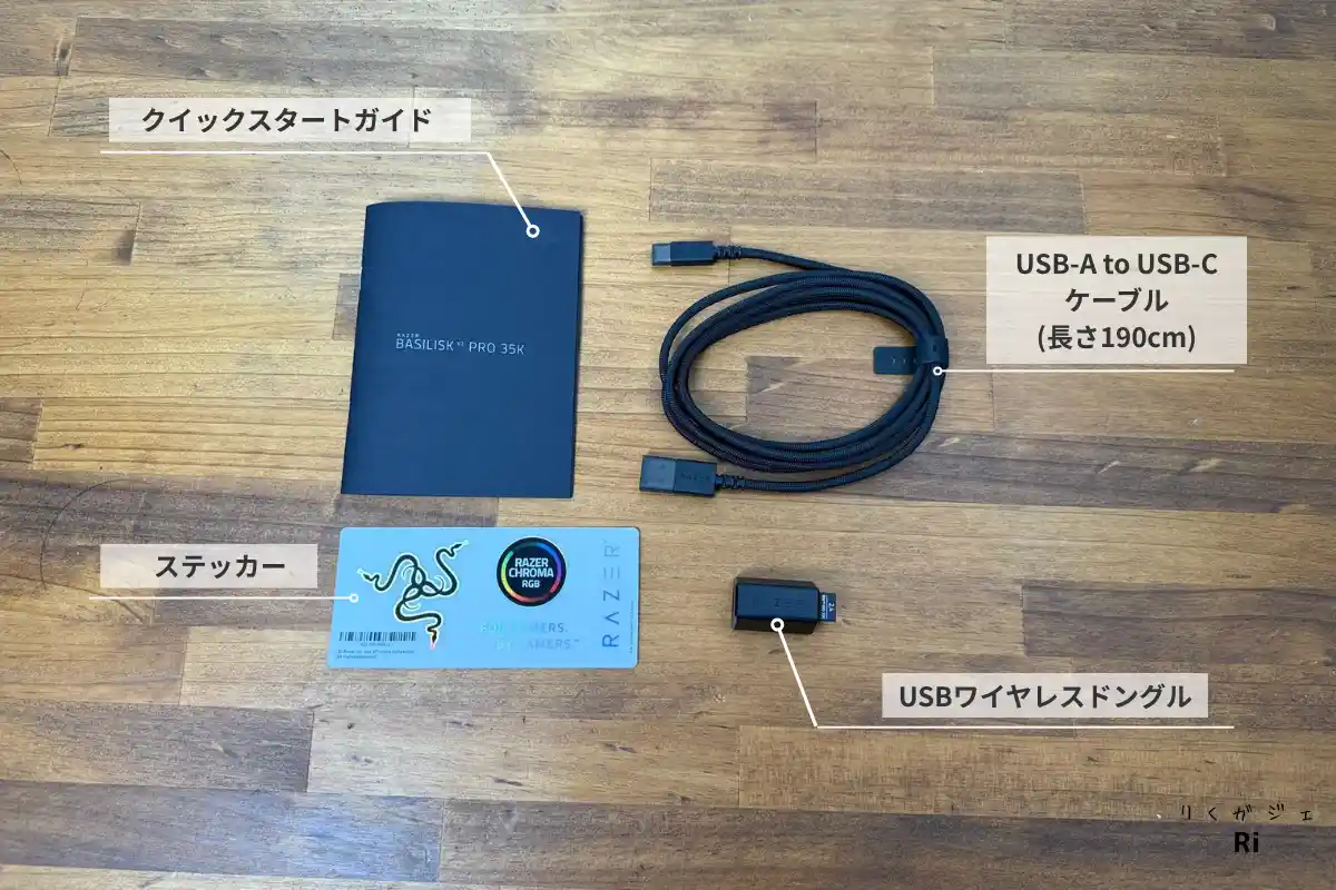 Razer Basilisk V3 Pro 35Kの付属品。USBワイヤレスドングル、USB-A to USB-Cケーブル(約190cm)、ステッカー、クイックスタートガイドが木目調のテーブルに並べられている