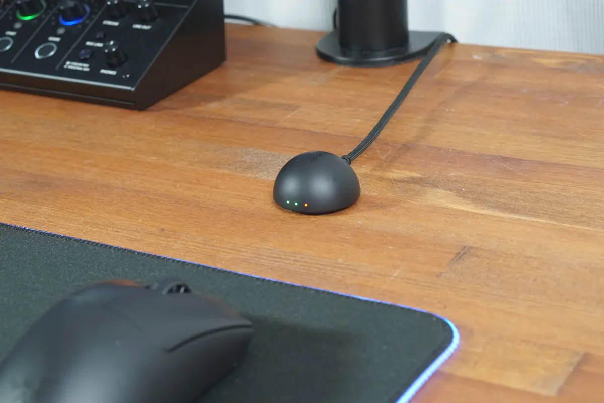 木目のデスク上に設置されたRazerのワイヤレスドングル。半球状でやや大きめの形状をしており、正面には3つの小さなインジケーターランプが点灯している。
