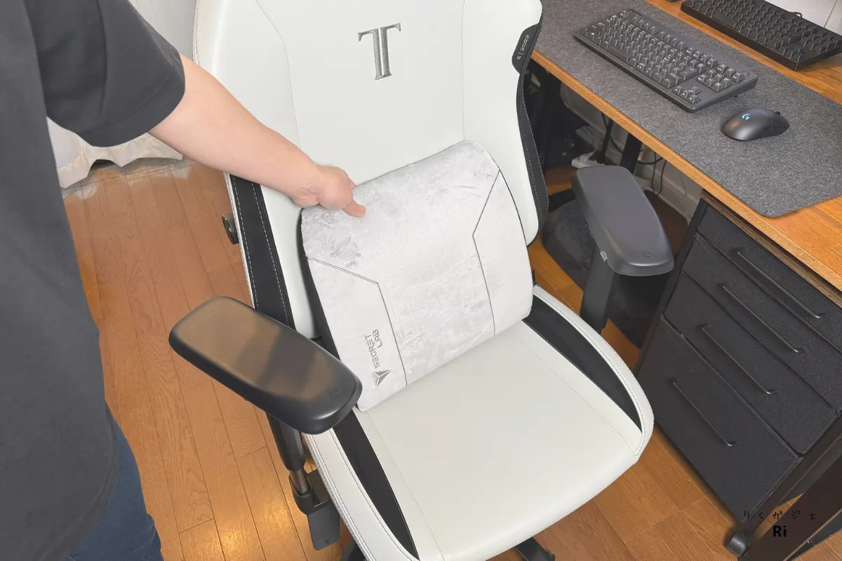 Secretlab TITAN Evoのチェアに、グレーのSecretlab純正ランバーピローを当てて設置しようとしている様子。ピローはやわらかいクッション素材で、腰へのサポート性を補うアイテムとして紹介されている。