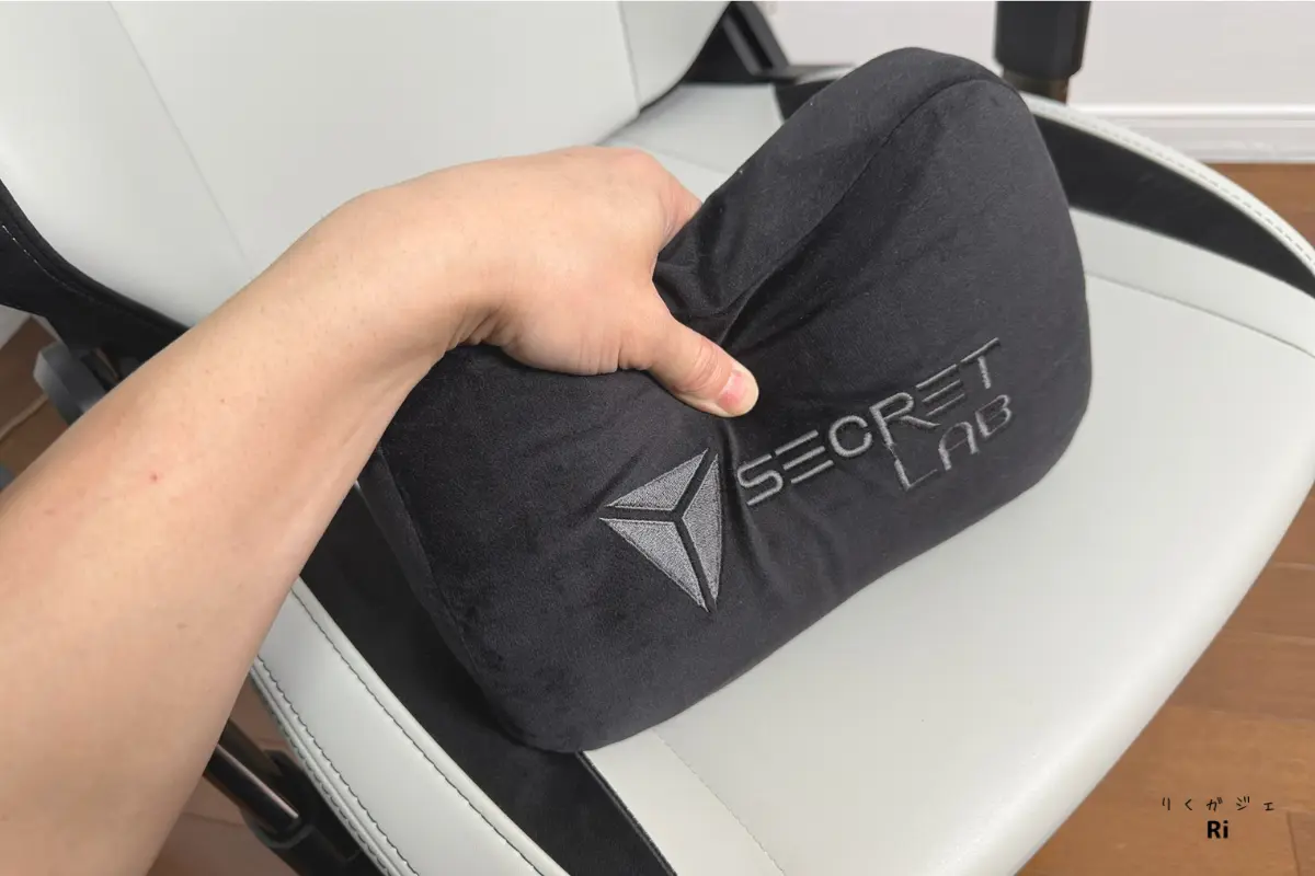 Secretlab TITAN Evoの座面上に、手で持ち上げられたSecretlab純正のランバーピローが置かれている。黒のクッションにはブランドロゴが刺繍され、チェアの白い座面とのコントラストが際立つ。