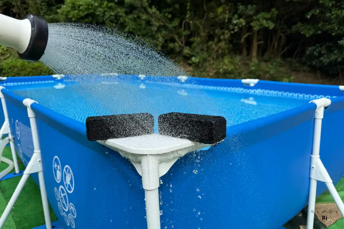 青い大型フレームプールに向けてシャワー状の水をかけ、防水性能をテストしている様子